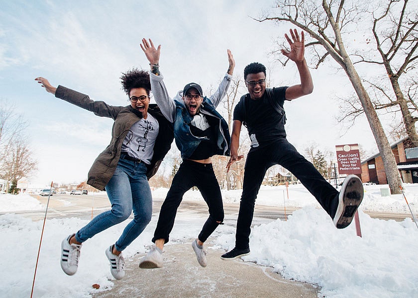 Three students jump around in the snow. 