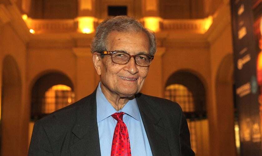 Image shows Amartya Sen in front of a university building.