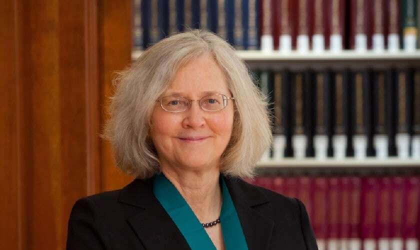 Image shows Elizabeth Blackburn in front of some bookcases. 