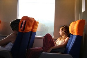 Image shows a young woman asleep on a train.